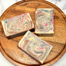 Load image into Gallery viewer, soap bar swirled with magenta, gold, white and brown colors on a brown tray
