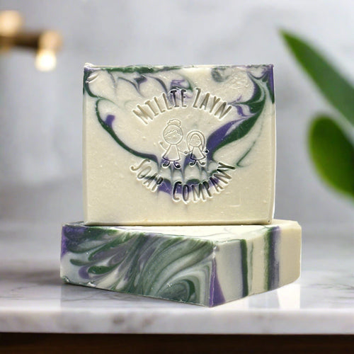 two soap bars. One is stacked on top of the other. They are white soap with swirls of green and purple